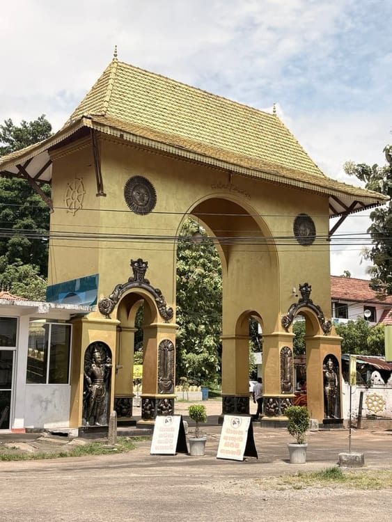 An ornate painted archway with sculpted mythical figures framing the entrance path to the temple