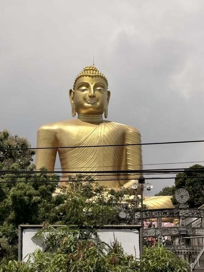 An enormous gilded seated Buddha figure rising above the treeline against a pale sky