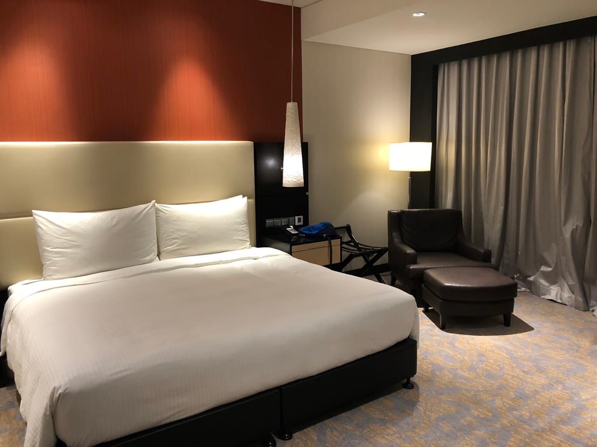 A made-up double bed in a city hotel room with bedside lamps lit and curtains drawn