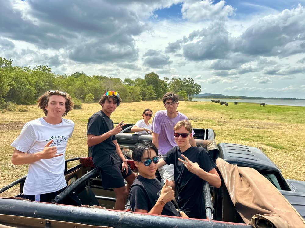 A group of guests in an open safari jeep parked beside the reservoir with grassland behind