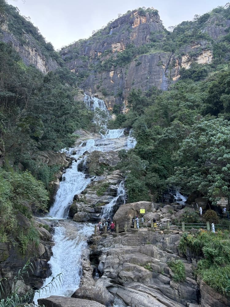 Water cascading over boulders at the Ravana Falls viewpoint with visitors on the rocks below