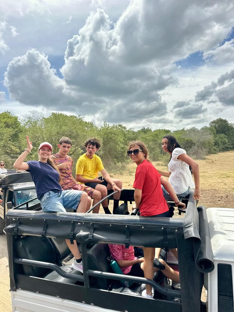 Group of guests standing beside a safari jeep on a dirt track after their morning drive