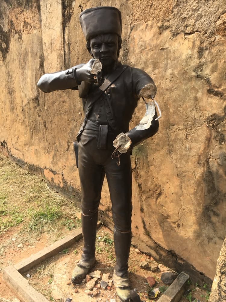 Dark bronze statue of a colonial-era soldier standing against the weathered rampart wall of Galle Fort