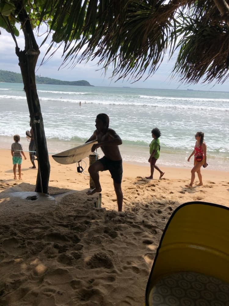 A surfer carrying a board down to the shore break on a busy south-coast beach near Galle