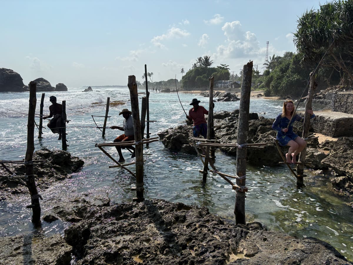 Stilt fishermen perched on wooden poles in the shallows off a rocky south-coast beach near Galle