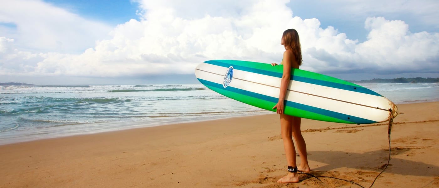 A surfer carrying a longboard down to the shoreline under a sky full of cloud
