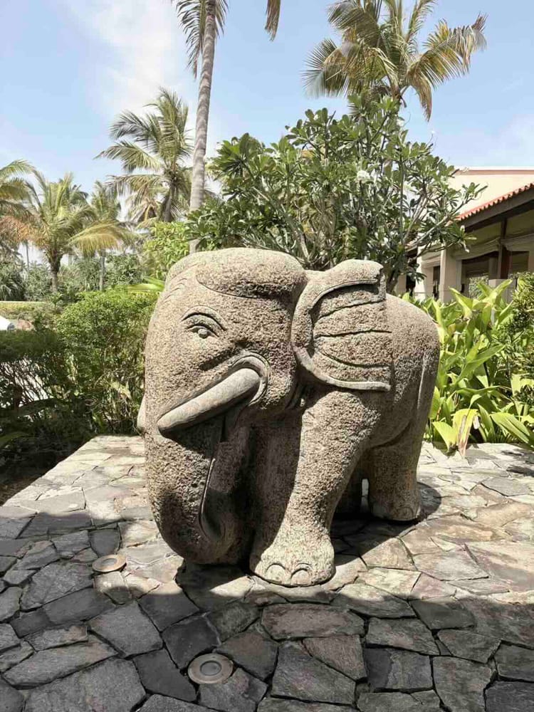 A large carved stone elephant with white tusks standing among tropical planting in the resort grounds