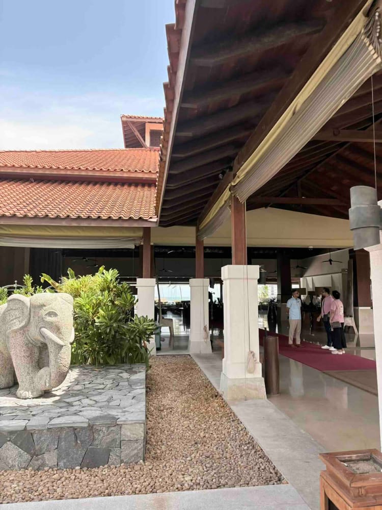 A stone elephant sculpture beside the open timber-roofed lobby entrance with guests arriving behind