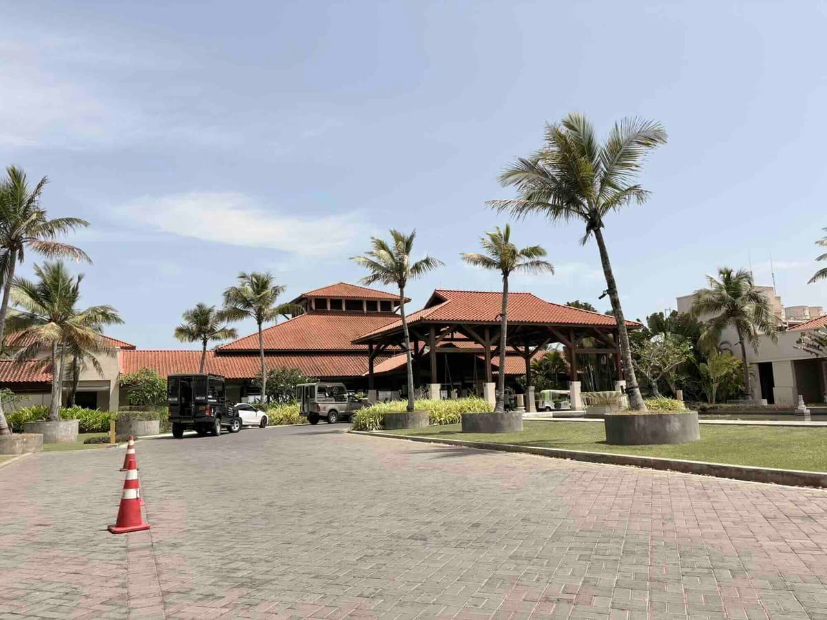 The pillared entrance canopy of the resort with buggies parked outside under a row of palm trees