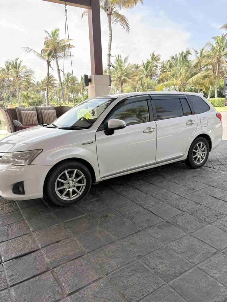 A white air-conditioned estate car parked on the paved forecourt beside a cushioned outdoor bench