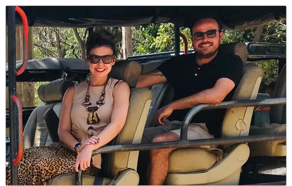 A couple sitting on the padded bench seats inside an open safari jeep, smiling towards the camera