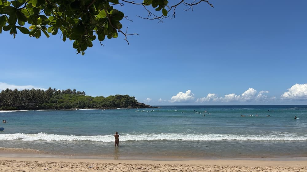 Swimmers in the sheltered horseshoe bay at Hiriketiya with a jungle headland behind