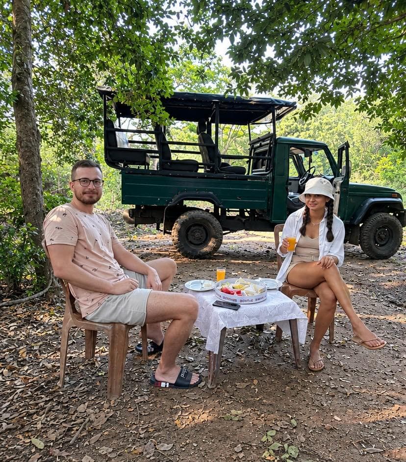 Two guests relaxing at a lunch table in the shade beside their open safari jeep on a full-day Udawalawe safari