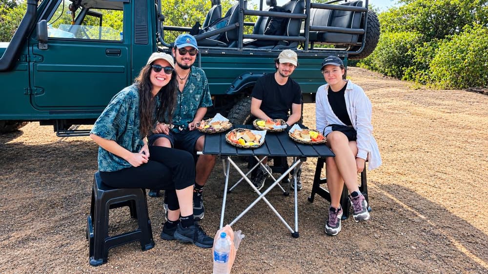 Four friends sharing a safari lunch at a folding table next to their private 4WD jeep
