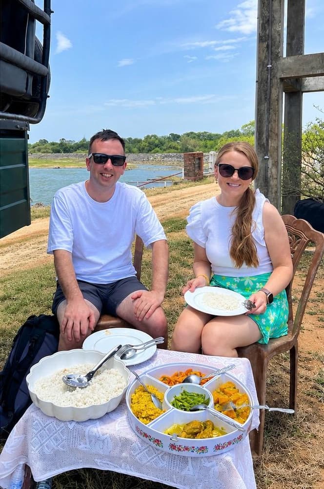Couple smiling at a picnic table by the water with bowls of rice and curry during a full-day safari lunch